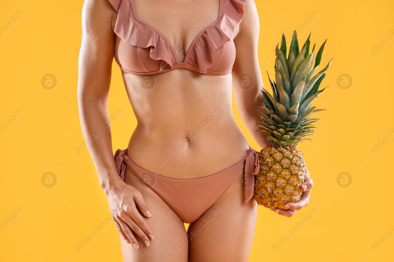 Photo of Woman in stylish bikini with fresh pineapple on orange background, closeup