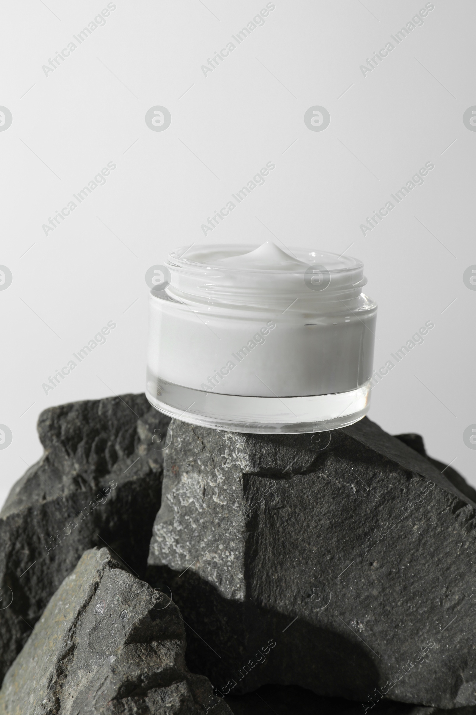 Photo of Face cream in jar on stones against light background