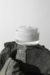 Face cream in jar on stones against light background