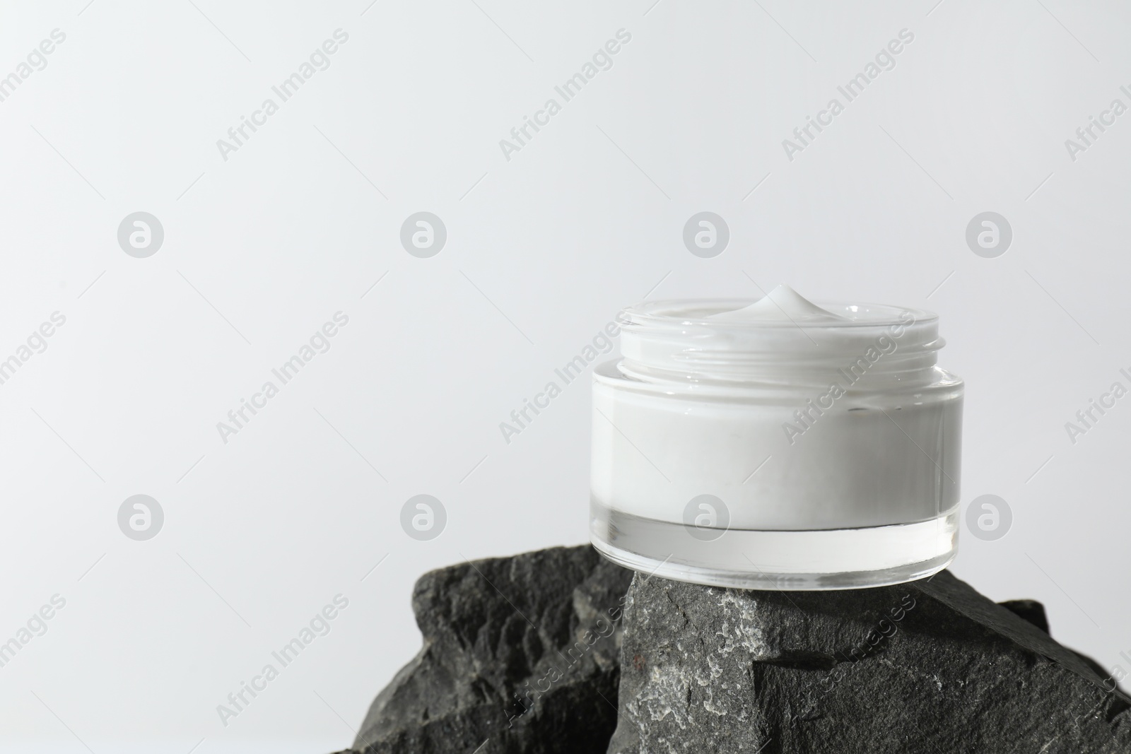 Photo of Face cream in jar on stone against light background, space for text