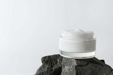 Face cream in jar on stone against light background, space for text