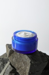 Face cream in jar on stones against light background