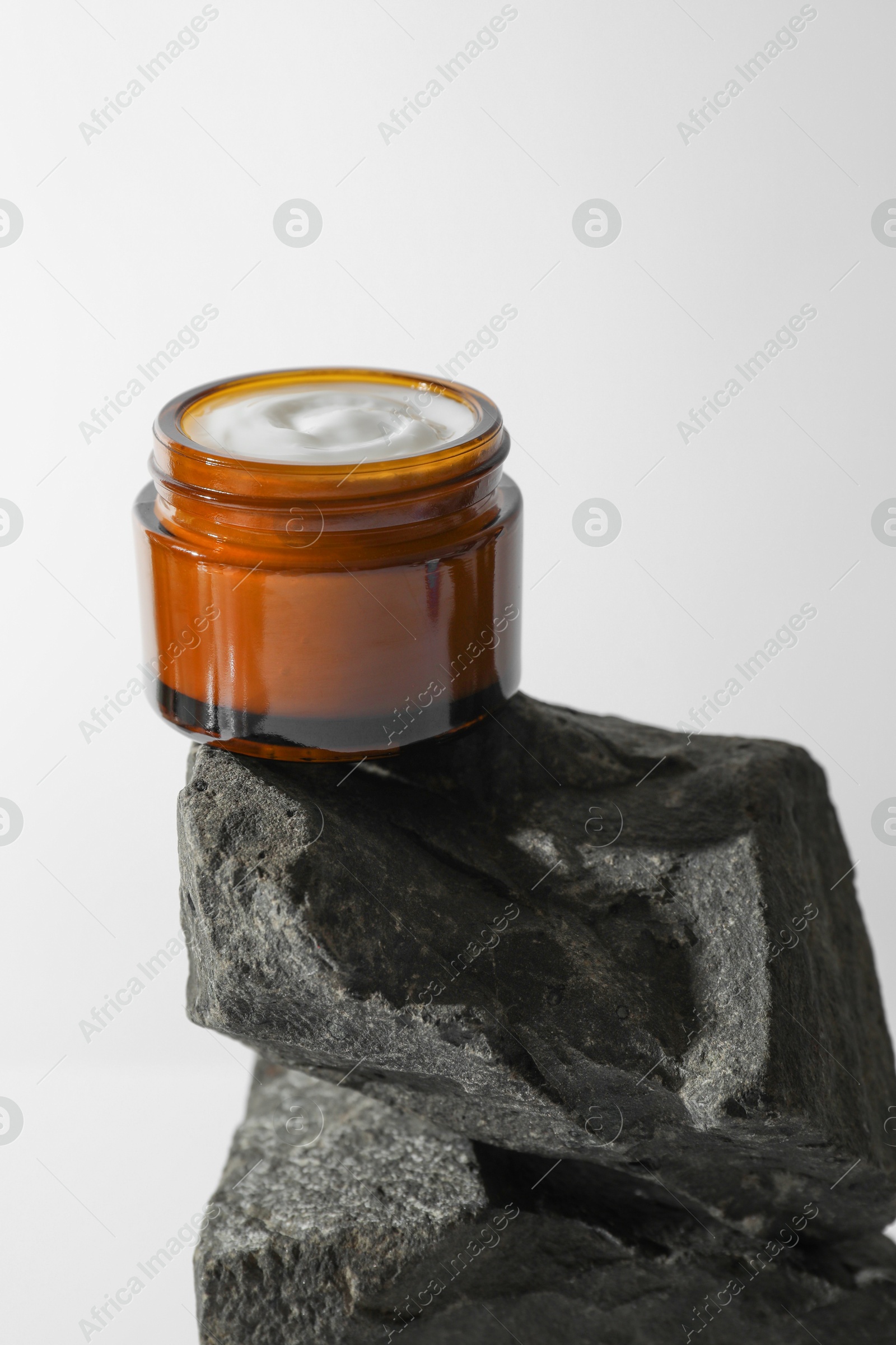 Photo of Face cream in jar on stones against light background