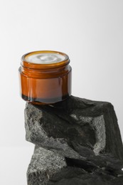 Photo of Face cream in jar on stones against light background