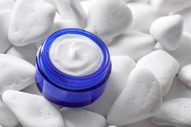 Photo of Face cream in jar on white stones, closeup. Cosmetic product