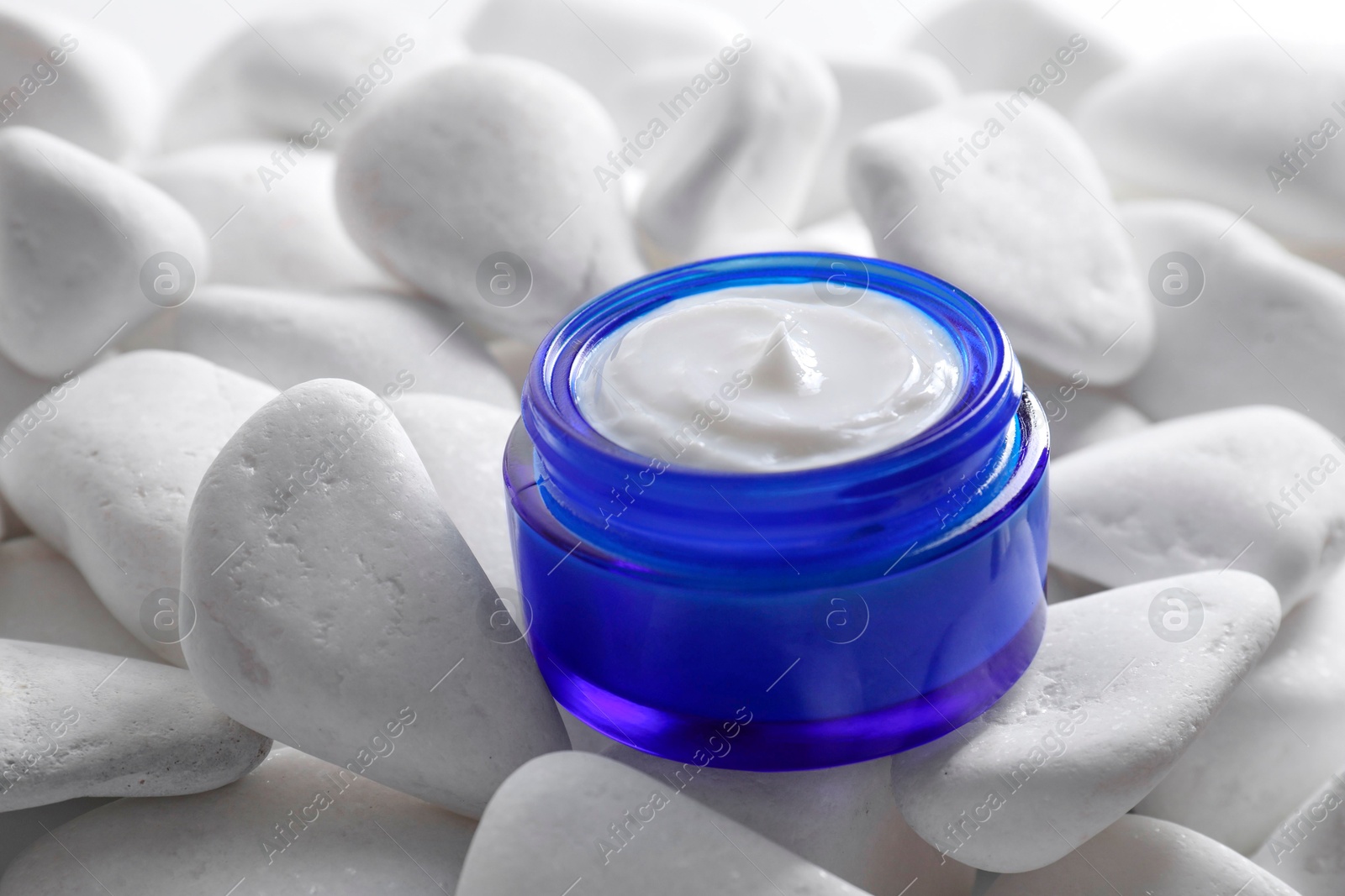 Photo of Face cream in jar on white stones, closeup. Cosmetic product