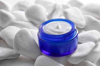 Face cream in jar on white stones, closeup. Cosmetic product