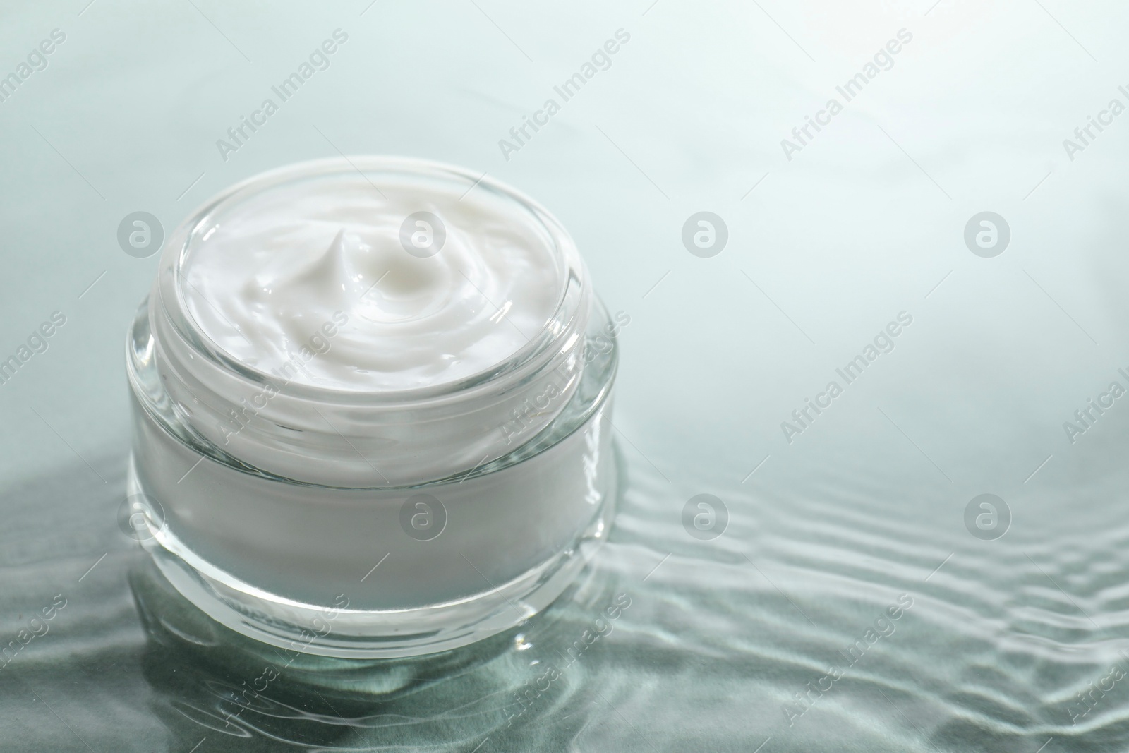 Photo of Jar with face cream in water on light green background, closeup. Space for text