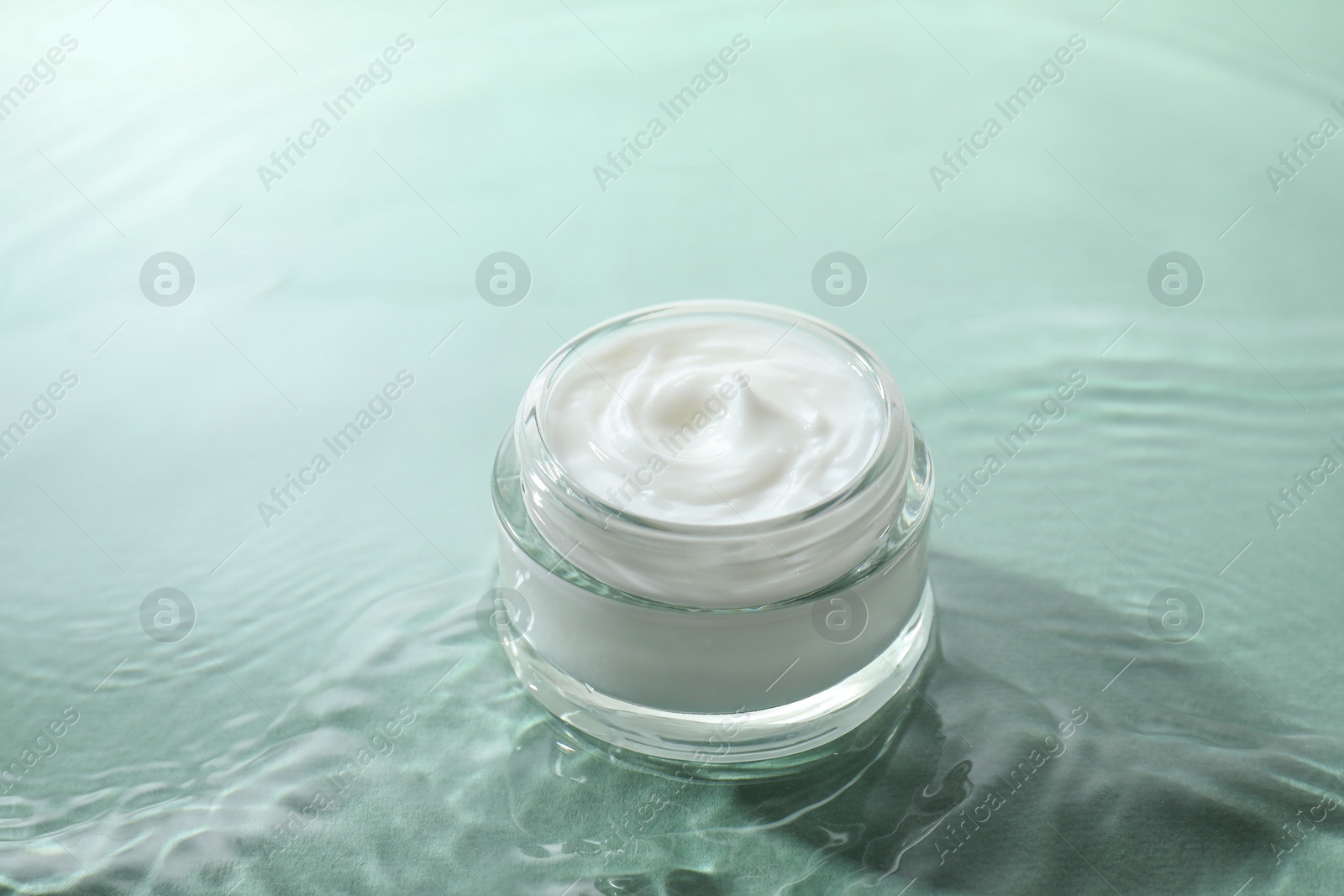 Photo of Jar with face cream in water on light green background