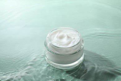 Photo of Jar with face cream in water on light green background