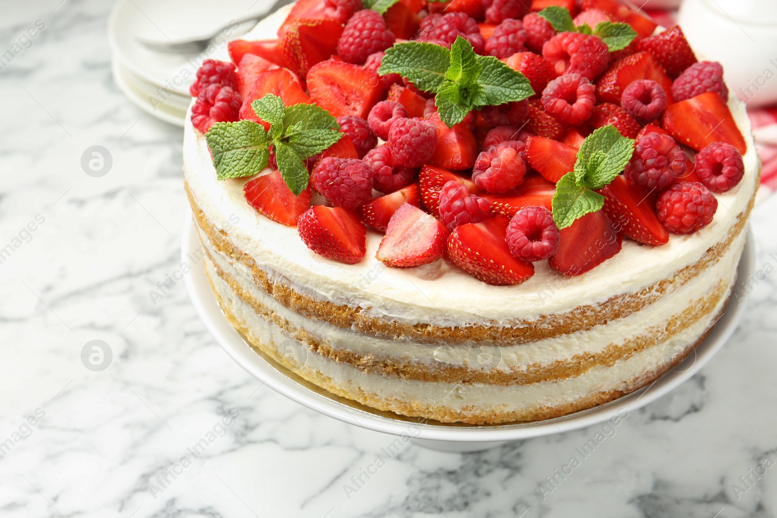 Photo of Tasty sponge cake with fresh berries and mint on white marble table, closeup