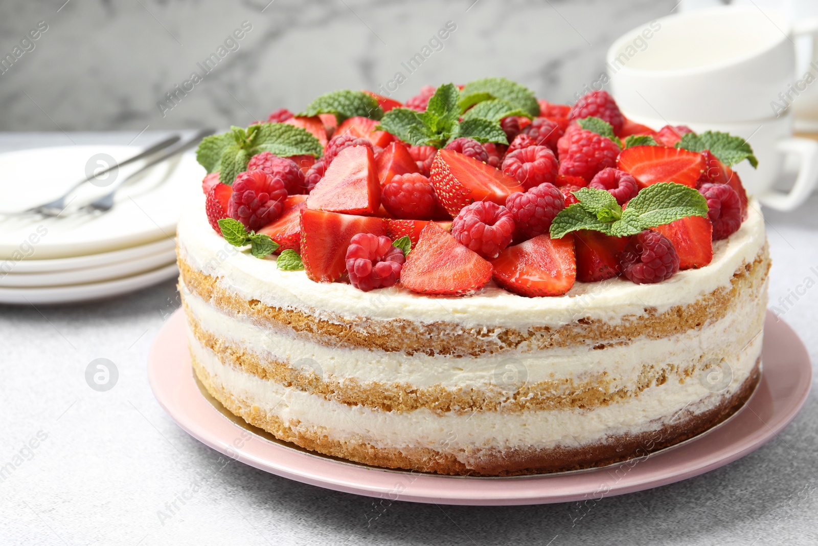 Photo of Tasty sponge cake with fresh berries and mint on light gray table