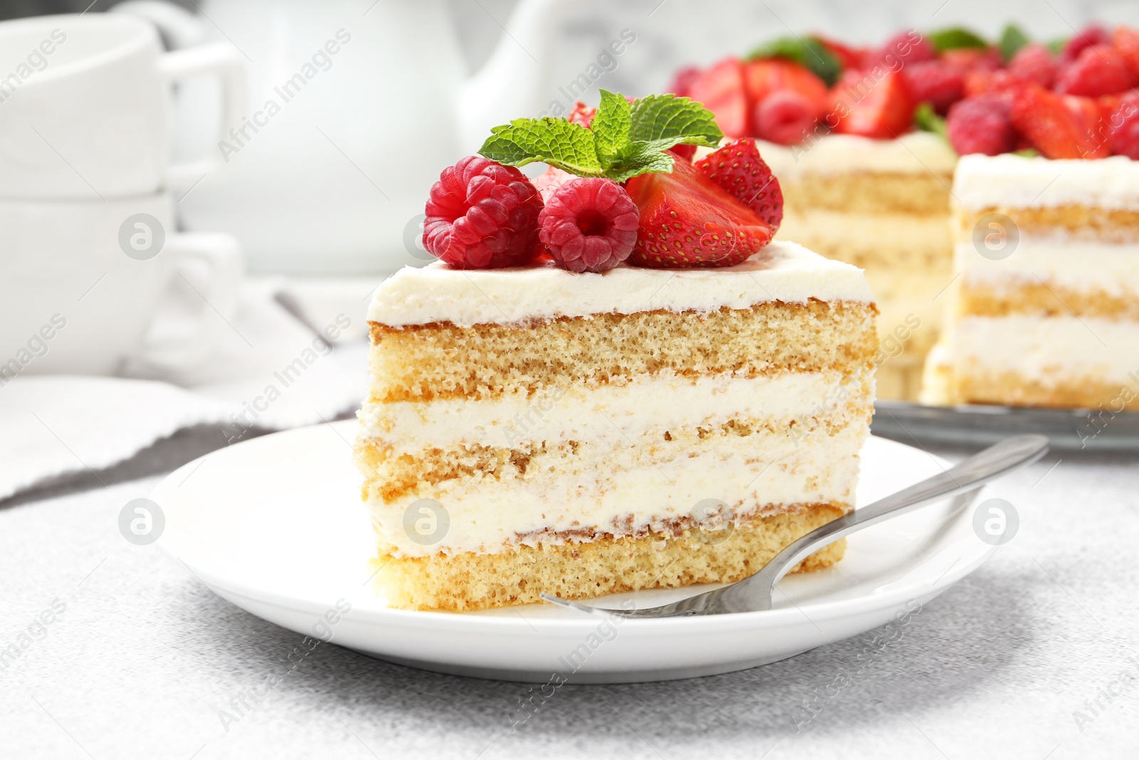 Photo of Tasty sponge cake with fresh berries and mint served on light gray table, closeup