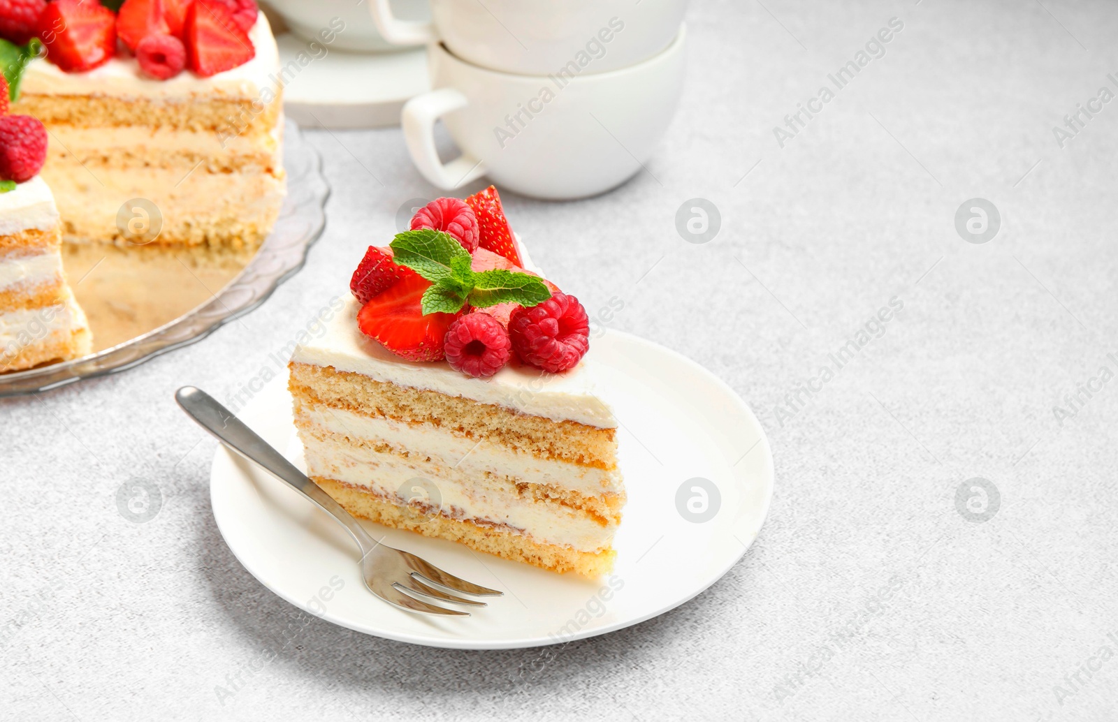 Photo of Piece of tasty sponge cake with fresh berries and mint served on light gray table, space for text