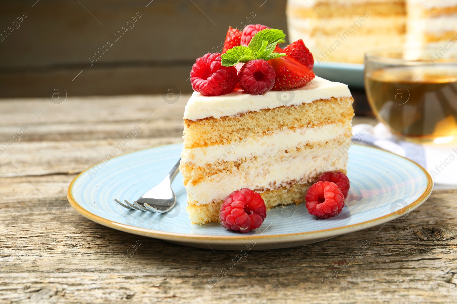 Photo of Piece of tasty sponge cake with fresh berries and mint served on wooden table