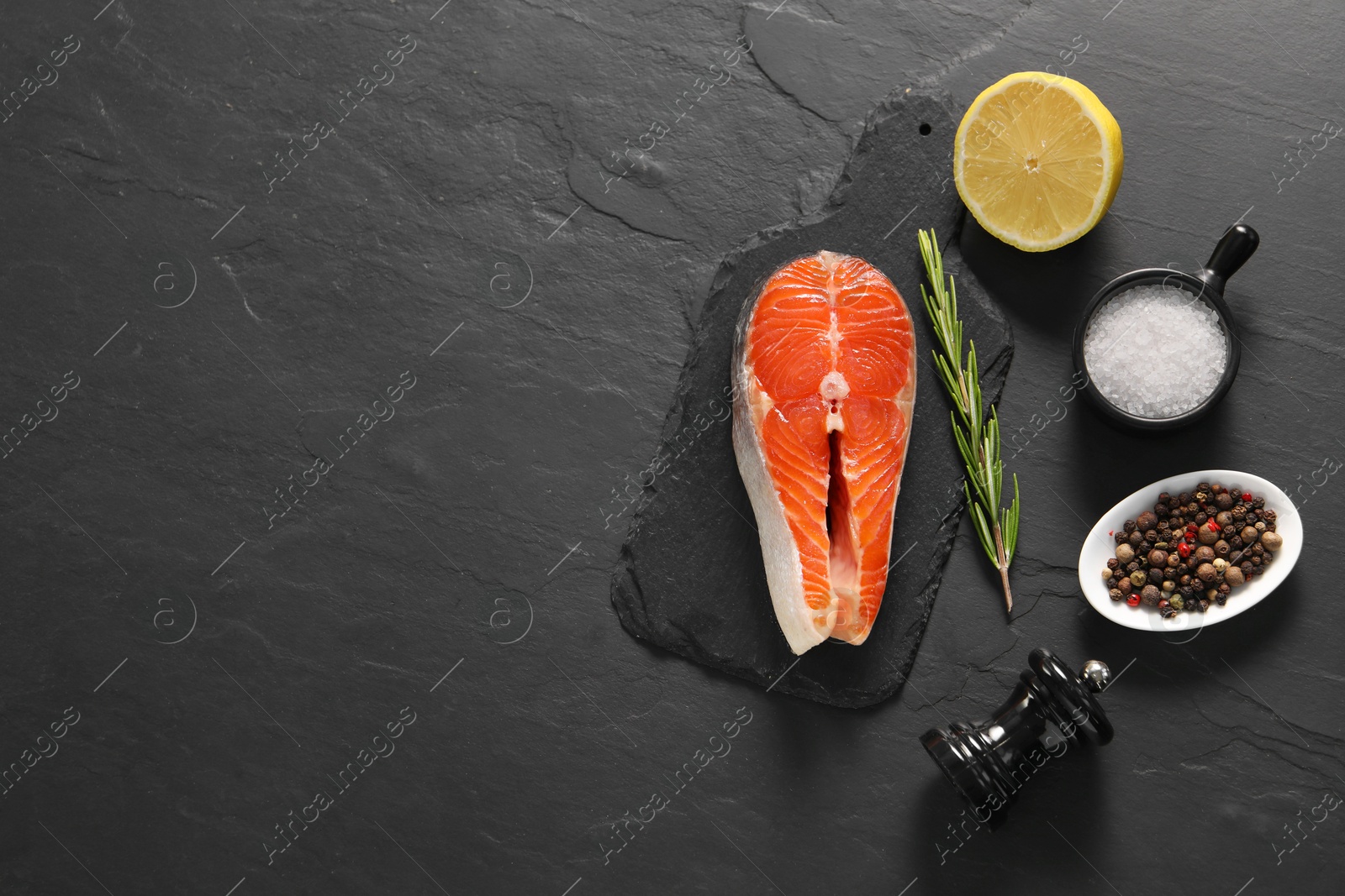 Photo of Fresh salmon steak, rosemary, lemon and spices on dark textured table, flat lay. Space for text