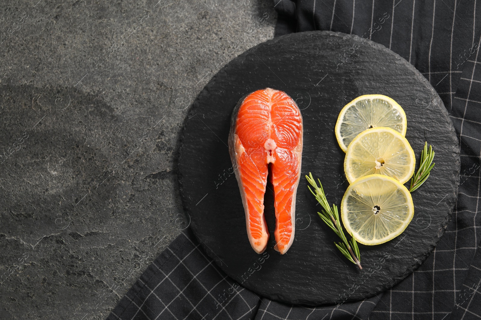 Photo of Fresh salmon steak, rosemary and lemon on dark textured table, top view. Space for text