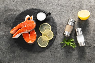 Photo of Fresh salmon steaks, lemon and spices on dark textured table, flat lay