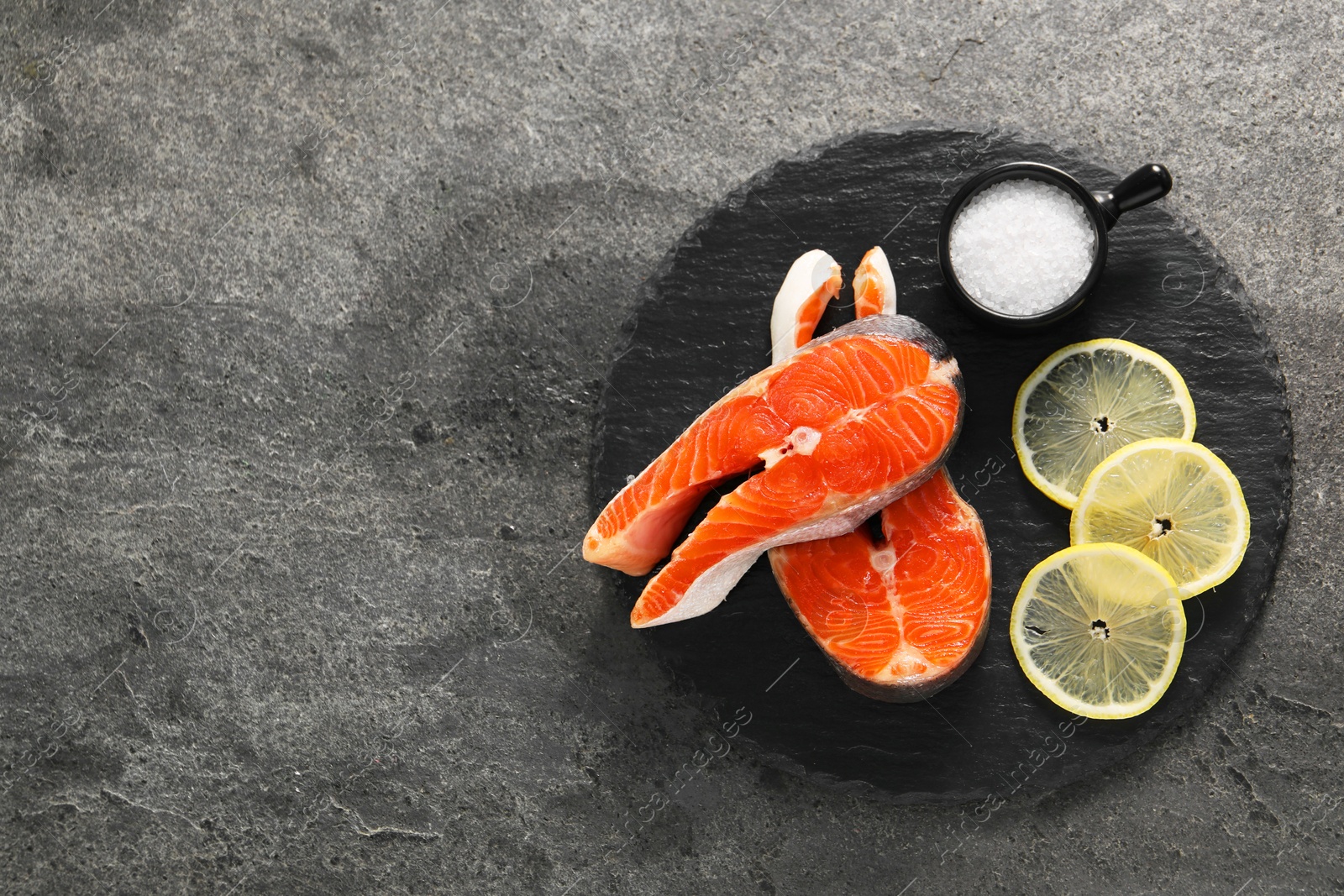 Photo of Fresh salmon steaks, salt and lemon on dark textured table, top view. Space for text