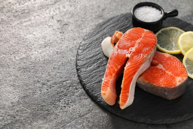 Photo of Fresh salmon steaks, salt and lemon on dark textured table, closeup. Space for text