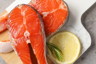 Photo of Board with fresh salmon steaks, rosemary and lemon on grey textured table, top view