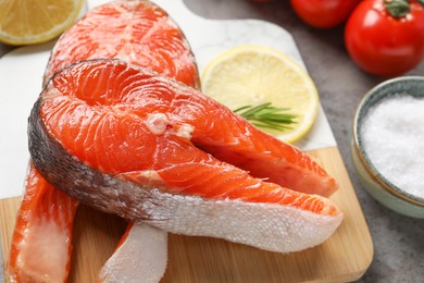 Photo of Board with fresh salmon steaks on grey textured table, closeup