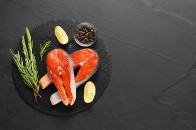 Photo of Fresh salmon steaks, rosemary, peppercorns and lemon on dark textured table, flat lay. Space for text