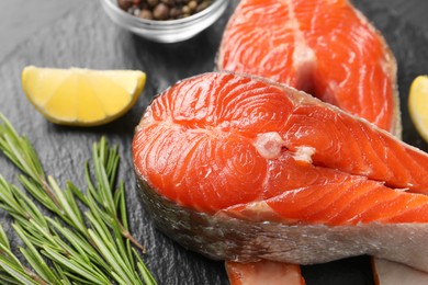 Photo of Fresh salmon steaks, rosemary and lemon on grey textured table, closeup