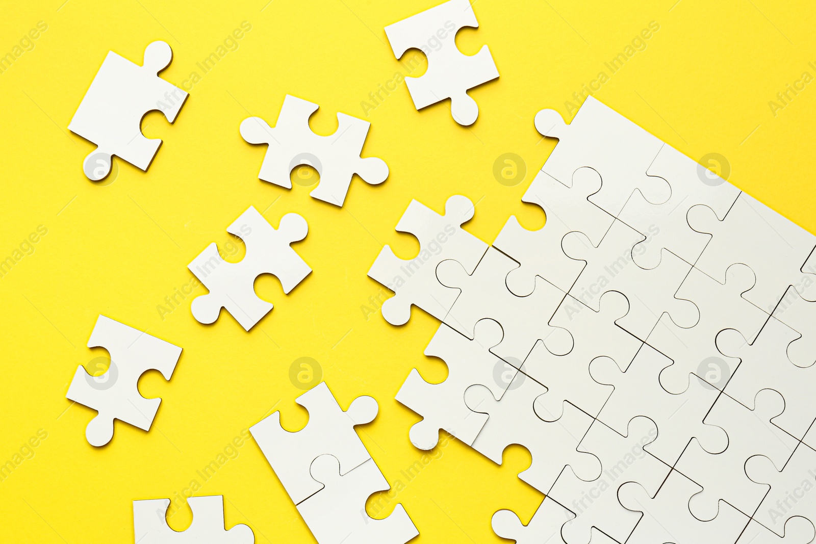 Photo of White puzzle pieces on yellow background, top view