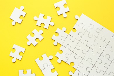 Photo of White puzzle pieces on yellow background, top view