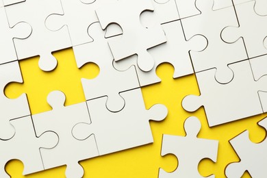 Photo of White puzzle pieces on yellow background, top view