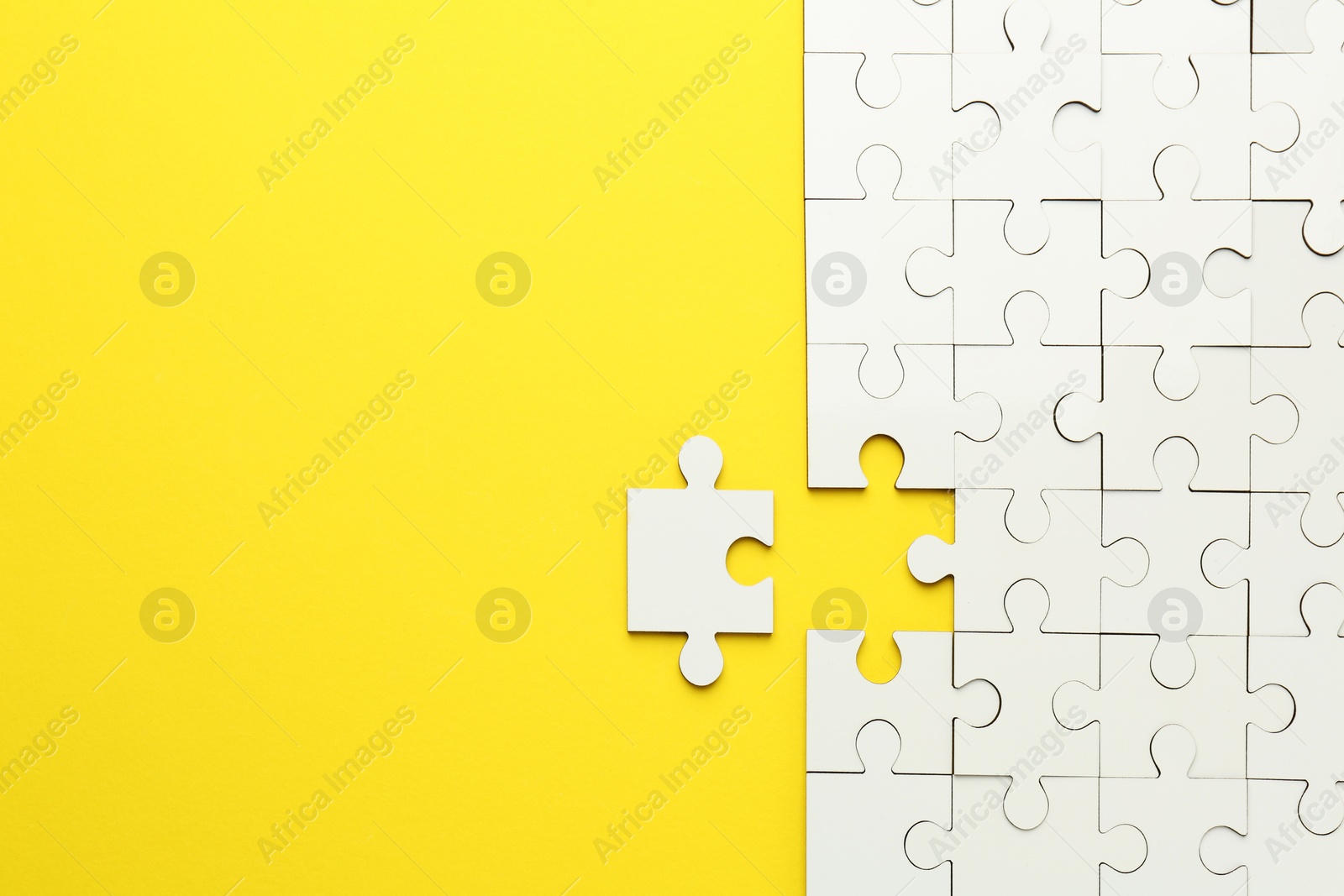 Photo of White puzzle pieces on yellow background, top view. Space for text