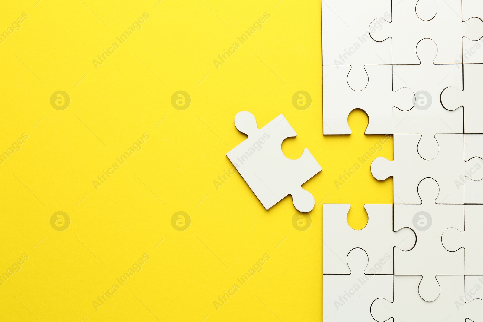 Photo of White puzzle pieces on yellow background, top view. Space for text