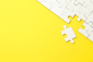 Photo of White puzzle pieces on yellow background, top view. Space for text