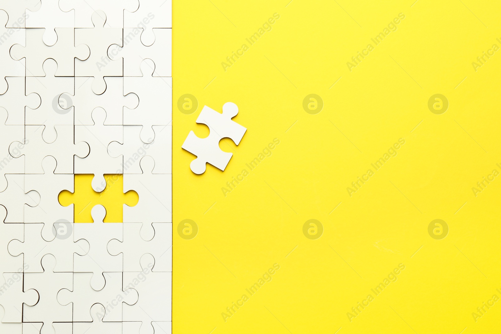 Photo of White puzzle pieces on yellow background, top view. Space for text