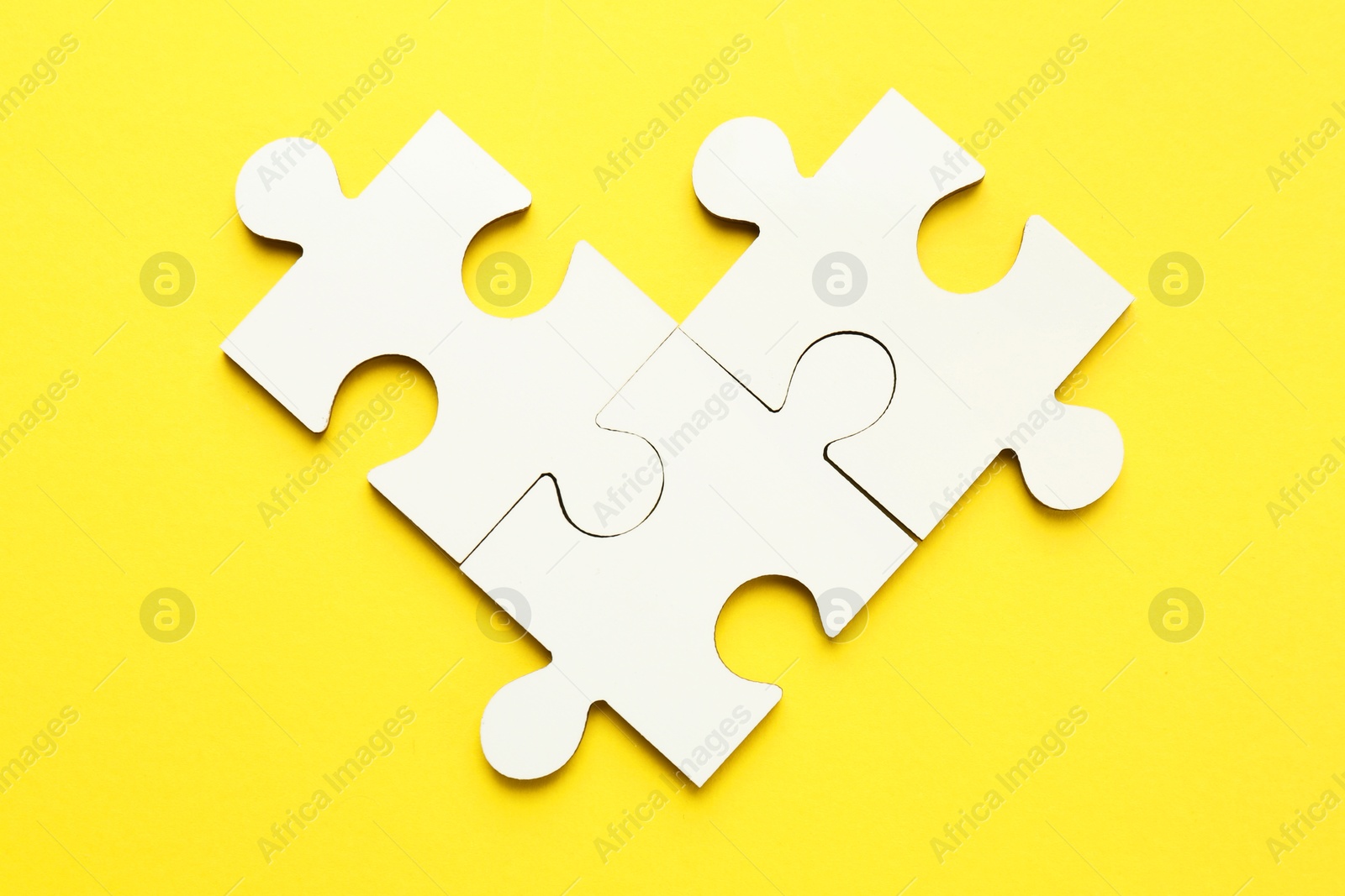 Photo of White puzzle pieces on yellow background, top view