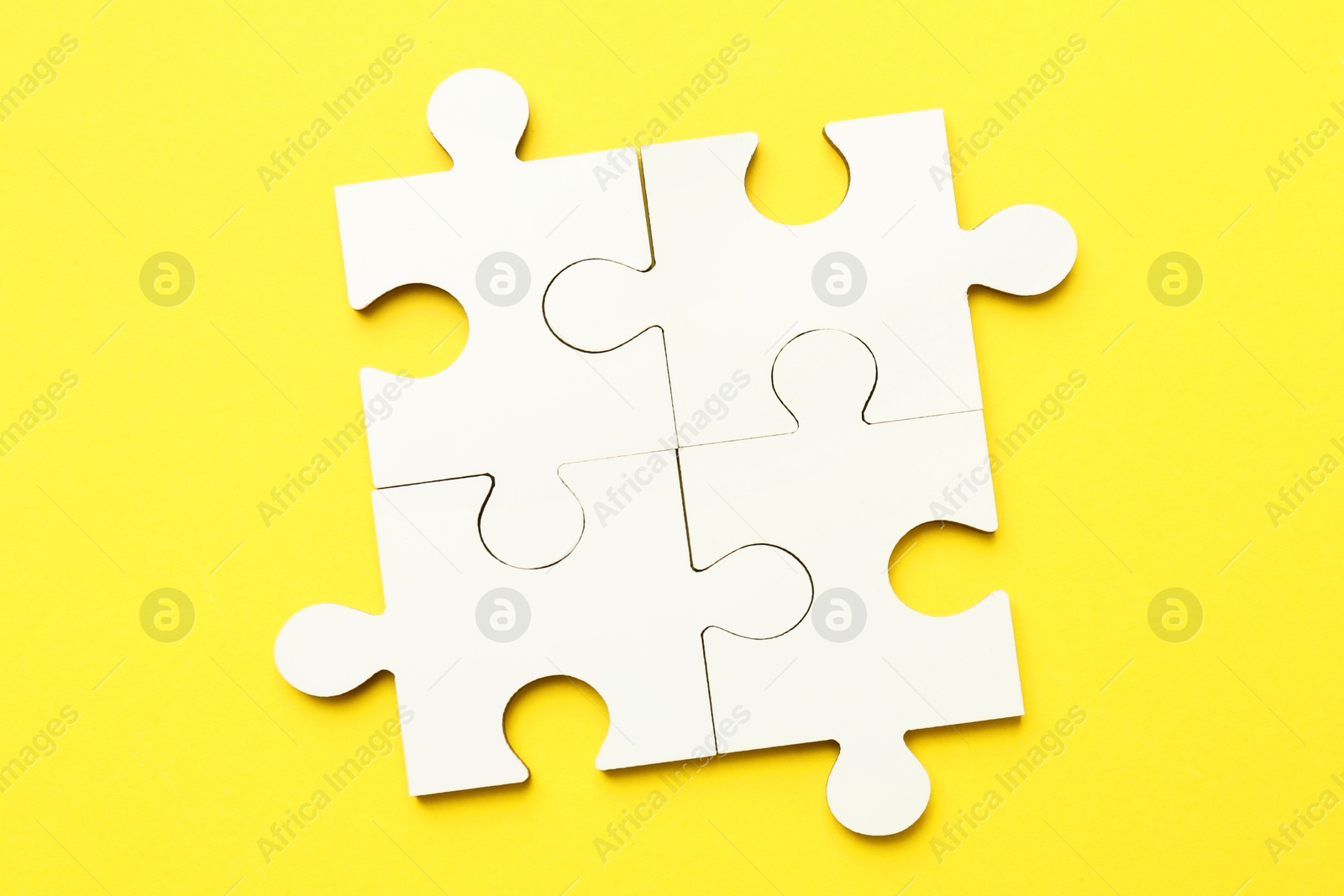 Photo of White puzzle pieces on yellow background, top view