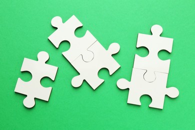 Photo of White puzzle pieces on green background, top view