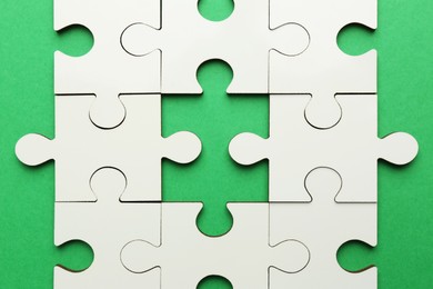 Photo of White puzzle pieces on green background, top view