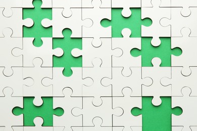 Photo of White puzzle with missing pieces on green background, top view