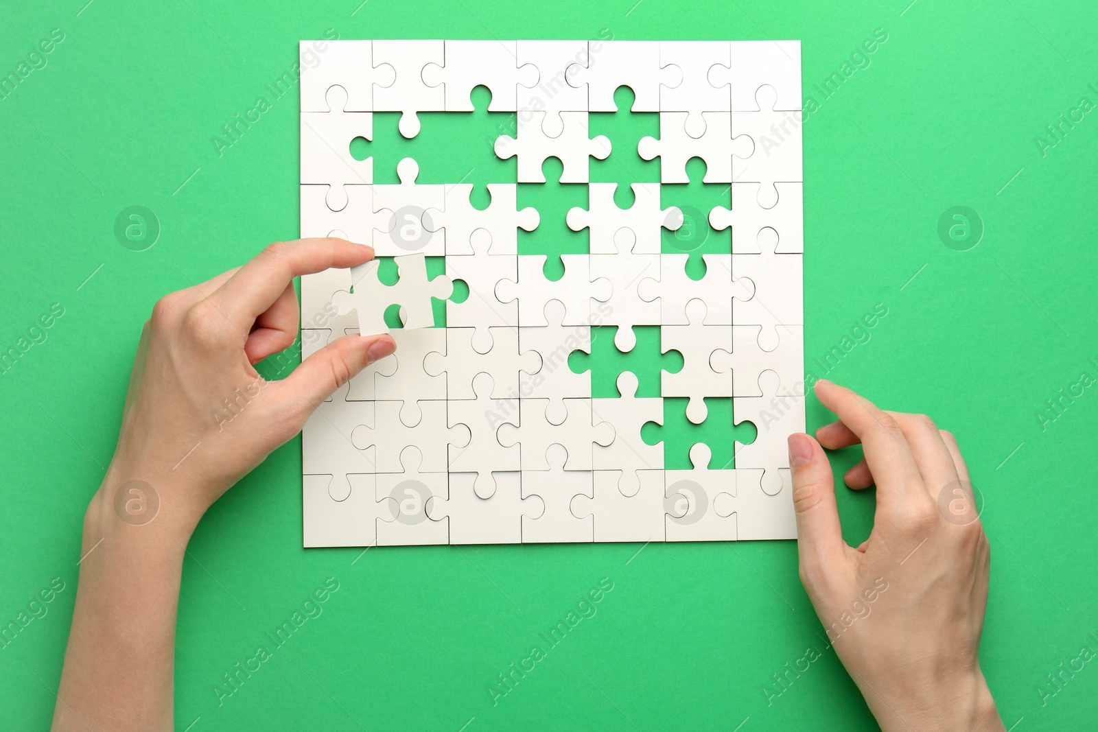 Photo of Woman solving white puzzle on green background, closeup