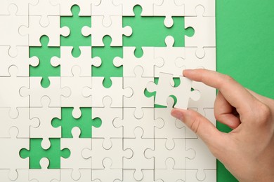 Photo of Woman solving white puzzle on green background, closeup