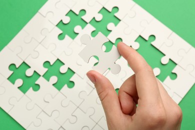 Photo of Woman solving white puzzle on green background, closeup