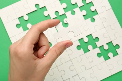 Woman solving white puzzle on green background, closeup