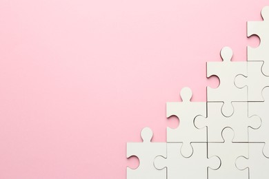 Photo of White puzzle pieces on pink background, top view. Space for text