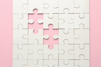 Photo of White puzzle with missing pieces on pink background, top view