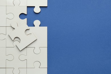 White puzzle pieces on blue background, top view. Space for text