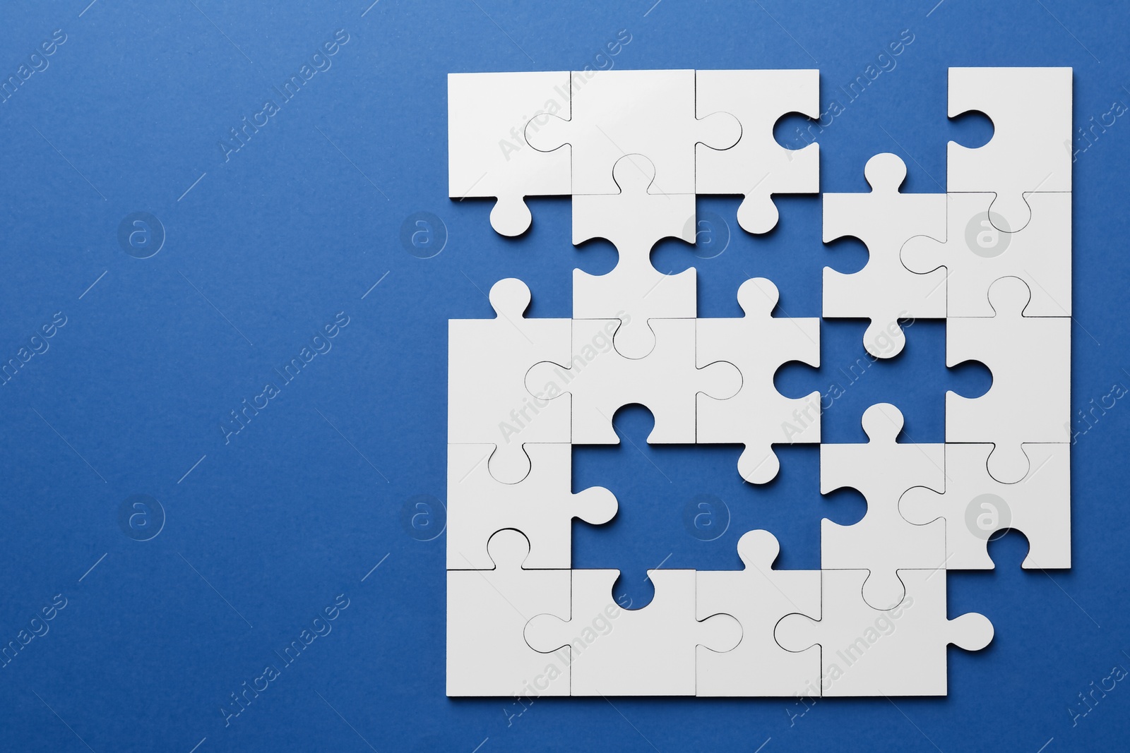 Photo of White puzzle with missing pieces on blue background, top view