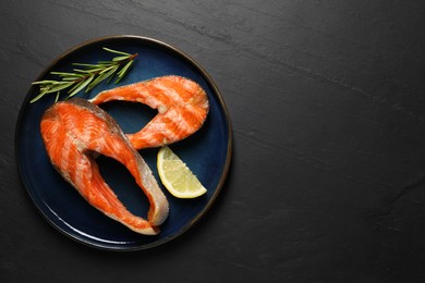 Photo of Tasty grilled salmon steaks, lemon and rosemary on black textured table, top view. Space for text