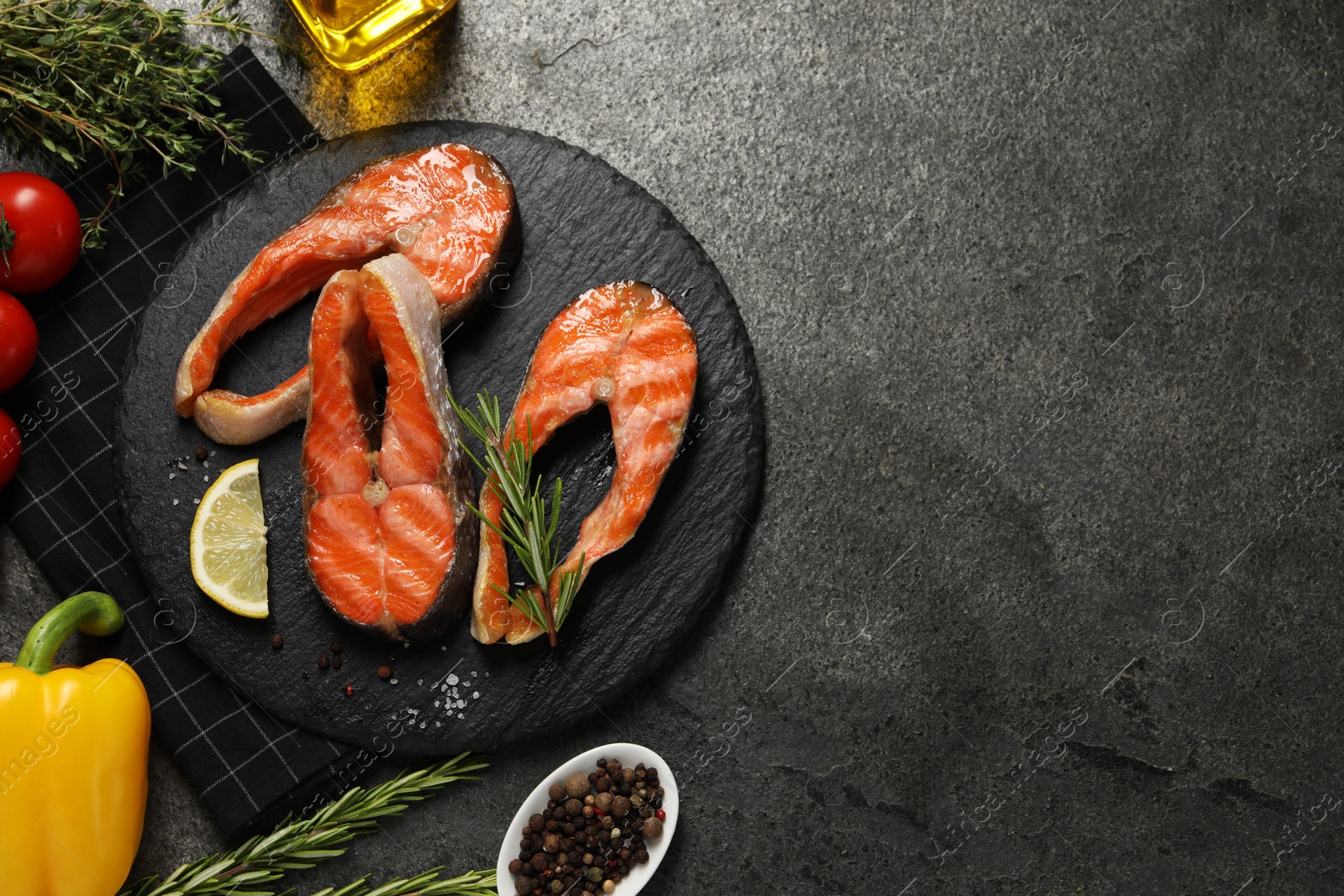 Photo of Tasty grilled salmon steaks, vegetables, oil and spices on gray textured table, flat lay. Space for text